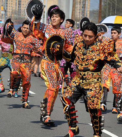 Des hommes en costume traditionnel se déplacent de manière dynamique dans la rue lors d'un défilé.