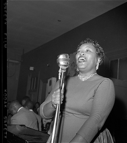 Photo en noir et blanc d'une femme chantant devant un microphone à l'ancienne.