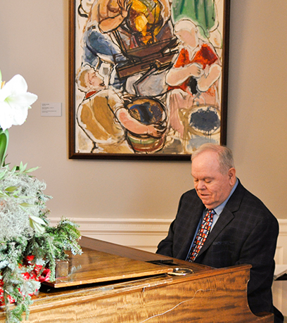 Un homme est assis derrière un piano avec un tableau en arrière-plan.