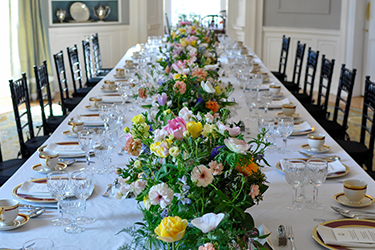 Table de salle à manger recouverte d'une nappe blanche et de fleurs sur toute la longueur de la table.
