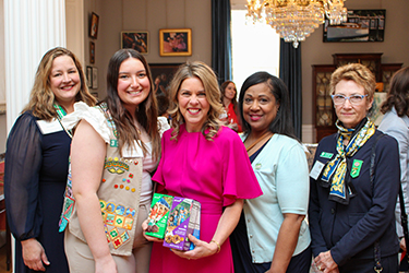 La Première dame pose en tenant des biscuits d'éclaireuses avec un groupe de femmes et une éclaireuse à l'intérieur du manoir.